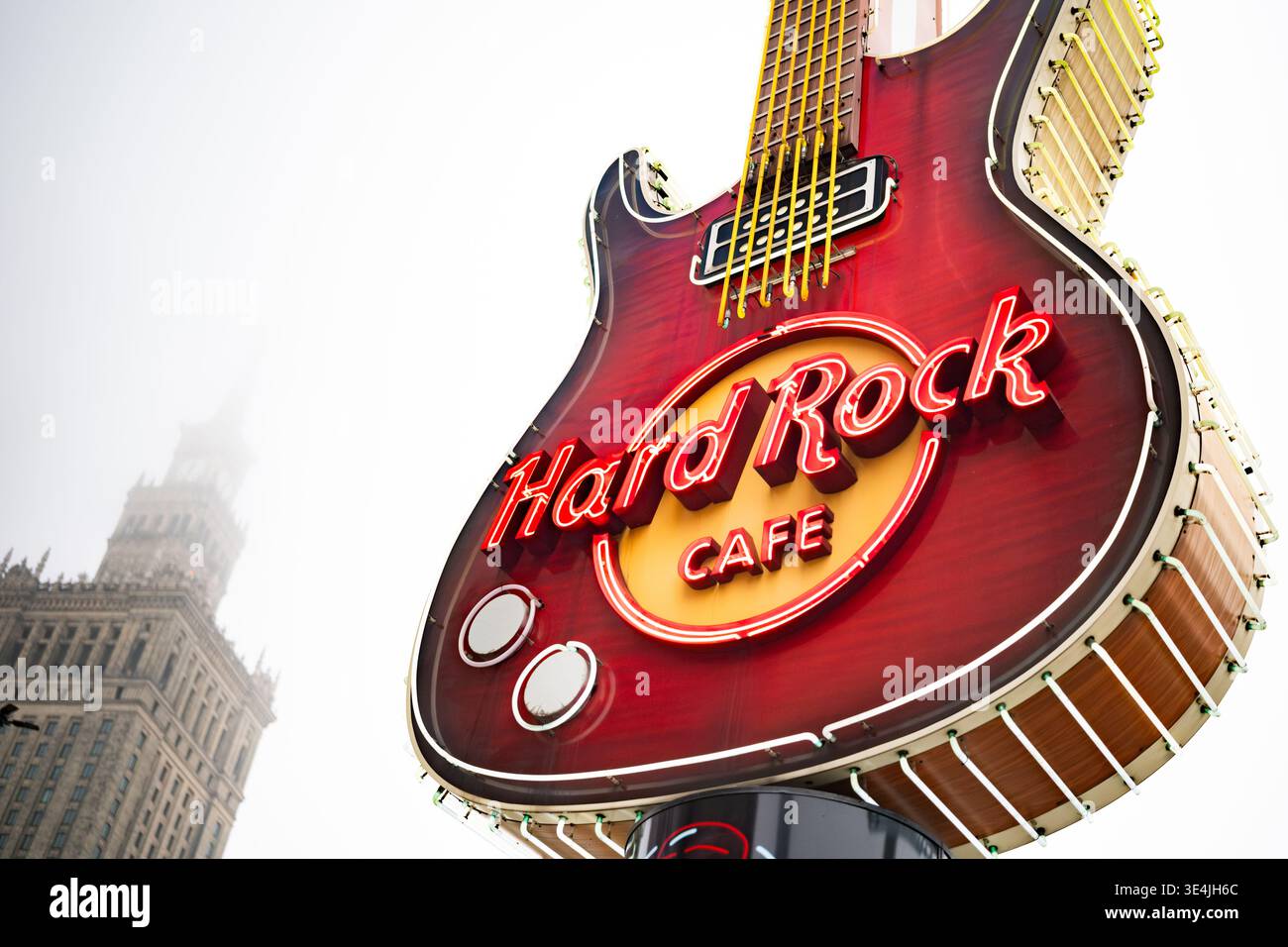 Varsavia, Polonia - 29 dicembre 2024: Big Neon Guitar serve come logo pubblicitario per l'Hard Rock Cafe sullo sfondo dell'edificio della Scienza e della Cultura di Varsavia Foto Stock