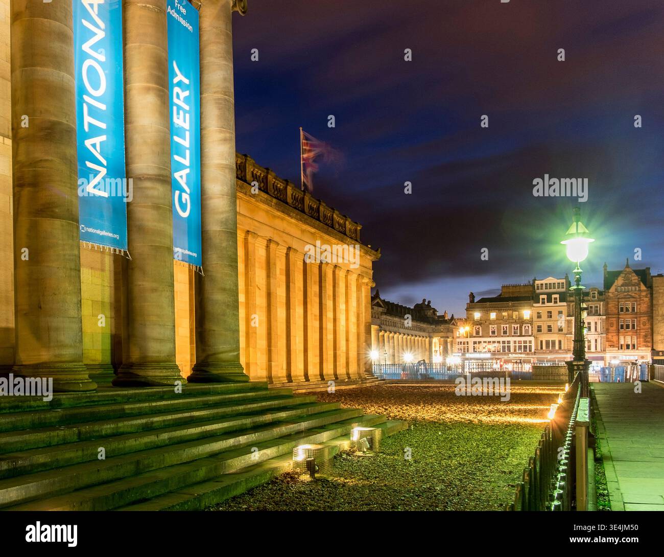 La National Gallery of Scotland di Edimburgo è immersa nella calda luce della sera, con colonne classiche, gradini in pietra e un'illuminante lampada da strada Foto Stock