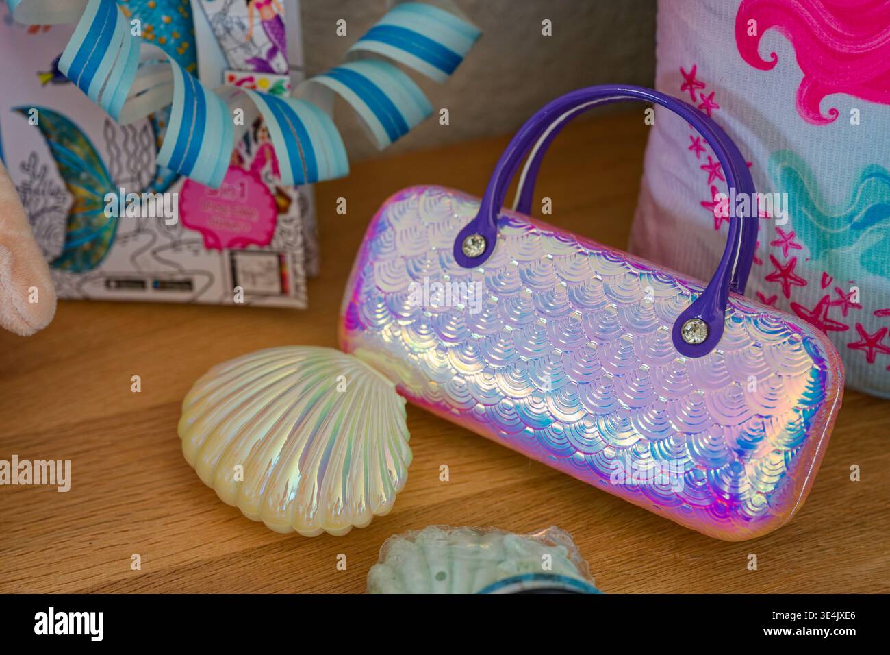 Una lucente borsa iridescente con motivo a scala sirena e manici viola si trova accanto a una decorazione perlescente della conchiglia su un tavolo di legno. Foto Stock