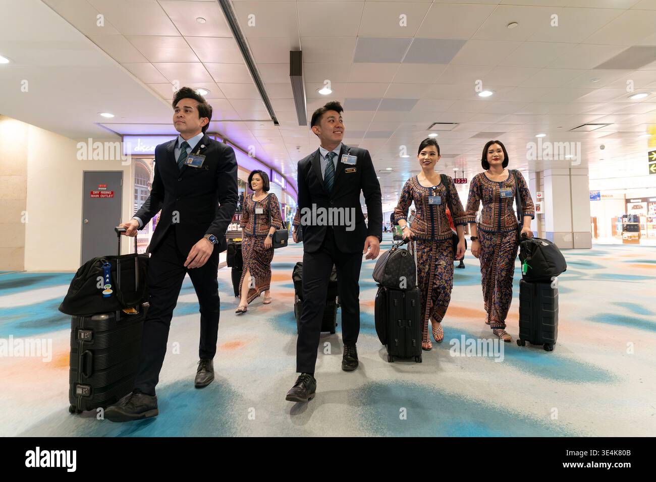 Singapore - 9 dicembre 2025: Un gruppo di membri di cabina della Singapore Airlines, di cui due maschi e quattro femmine, attraversa l'aeroporto di Changi con spirito Foto Stock
