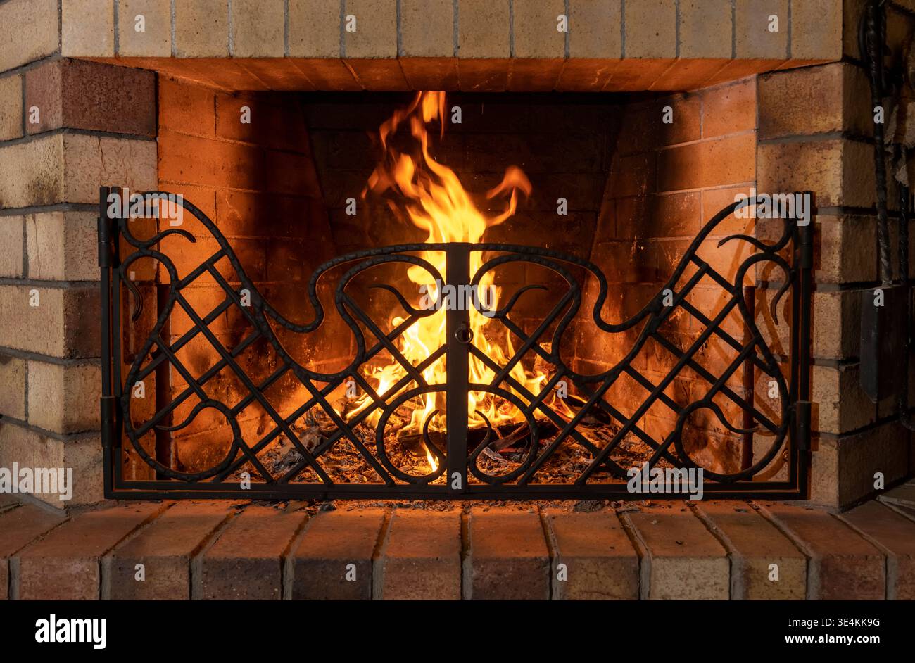 fiamme in un camino di casa in mattoni con una griglia forgiata in metallo, con illuminazione soffusa Foto Stock
