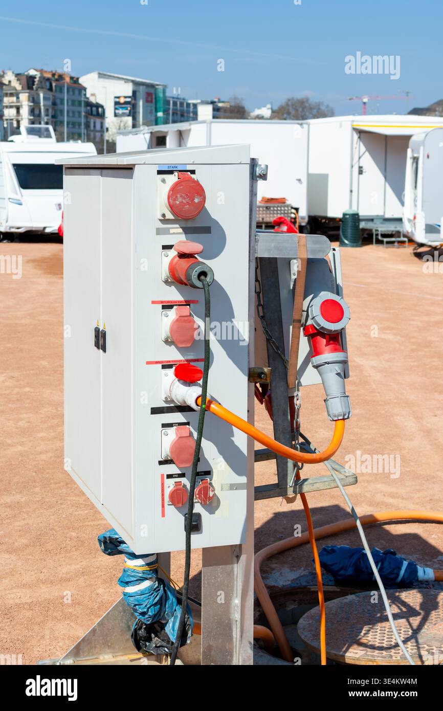 Montante portatile per utenze con prese di alimentazione industriali accanto ai punti di accesso aperti per la manutenzione in un'area temporanea di caravan e supporto del rimorchio su un terreno polveroso Foto Stock