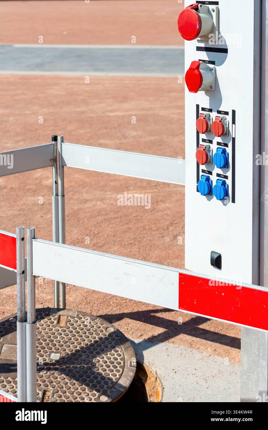 Vista laterale ravvicinata di un piedistallo per servizi elettrici temporanei con prese industriali accanto a un punto di accesso protetto per utenze presso un servi caravan esterno Foto Stock