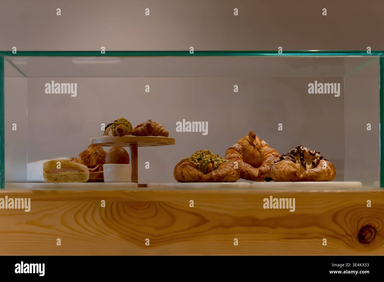 Selezione di croissant e dolci al forno disposti all'interno di una vetrina di vetro pulita su un banco di panetteria in legno. Foto Stock