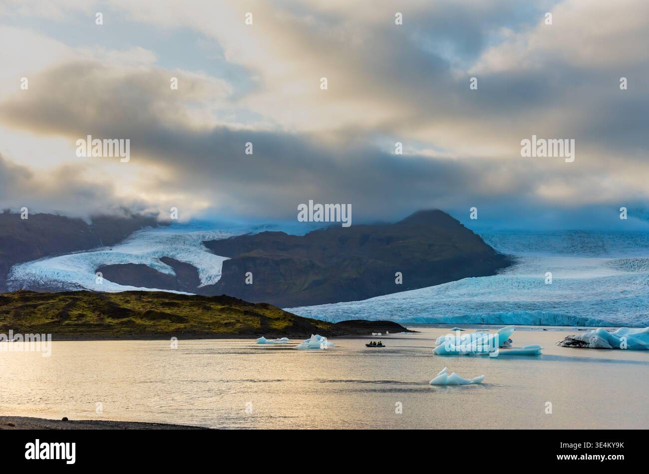 La laguna glaciale di Fjallsarlon presenta iceberg che galleggiano in acque calme, riflettendo il soffice bagliore del crepuscolo sullo sfondo del massiccio ghiacciaio. An Foto Stock
