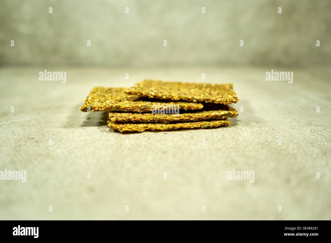 Una pila di cracker con semi multipli o pane croccante disposti su una superficie di cemento leggermente ruvida. I cracker dorati sono caratterizzati da semi visibili Foto Stock