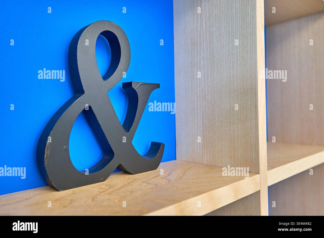 Un grande simbolo decorativo di colore grigio scuro si erge su una mensola di legno chiaro contro una parete blu vibrante. A destra, una libreria di legno con Foto Stock