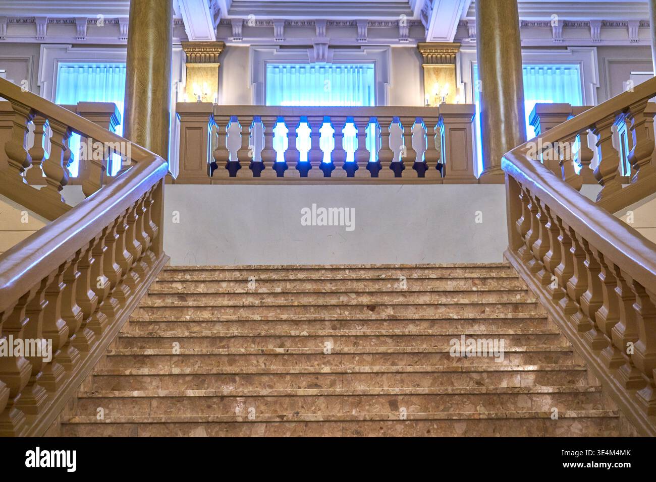 Una grande scalinata in marmo biforcato con ringhiere in legno ornate e balaustre all'interno di un edificio storico. La scala simmetrica presenta Foto Stock