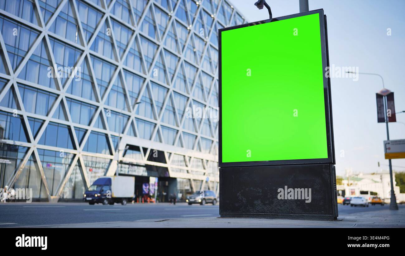 Cartellone con schermo verde per il mockup pubblicitario sulla strada urbana con un edificio moderno Foto Stock