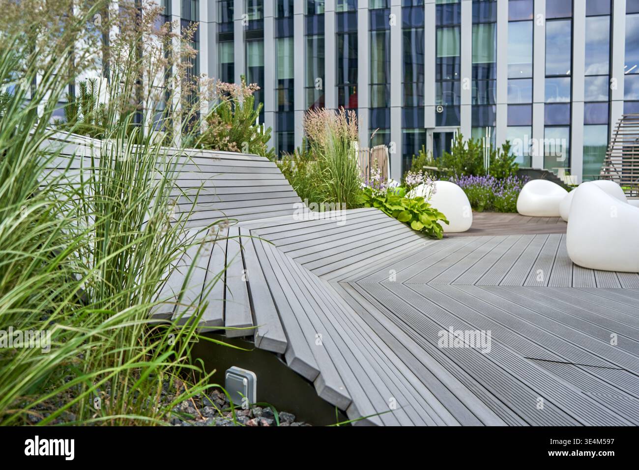 Una terrazza esterna contemporanea con pavimento in legno composito grigio, disposta in un distintivo motivo chevron, con panca curva integrata Foto Stock