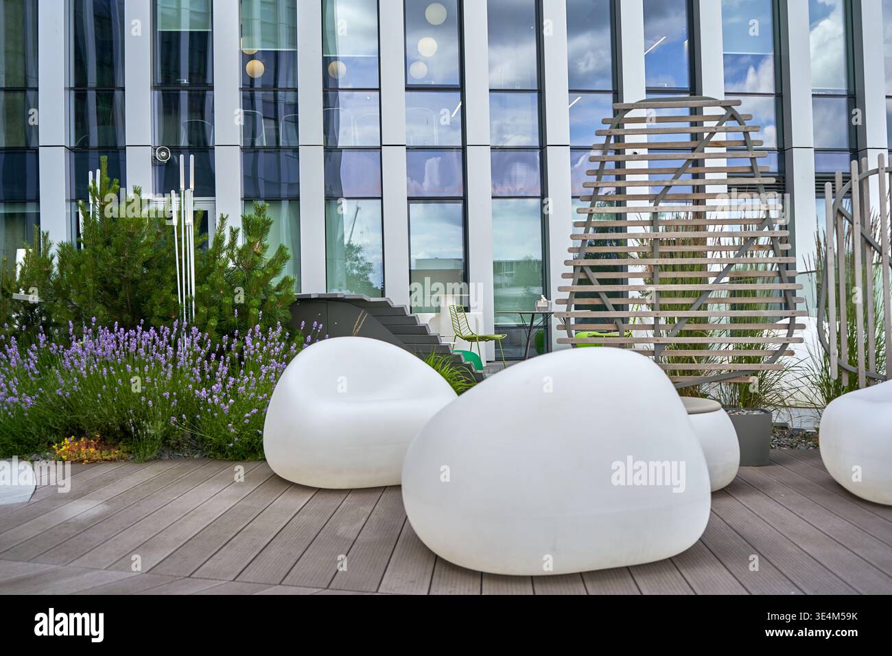 Una terrazza esterna contemporanea con posti a sedere bianchi a forma di ciottoli disposti su una terrazza in legno. Lo spazio include verde paesaggistico con lavanda Foto Stock