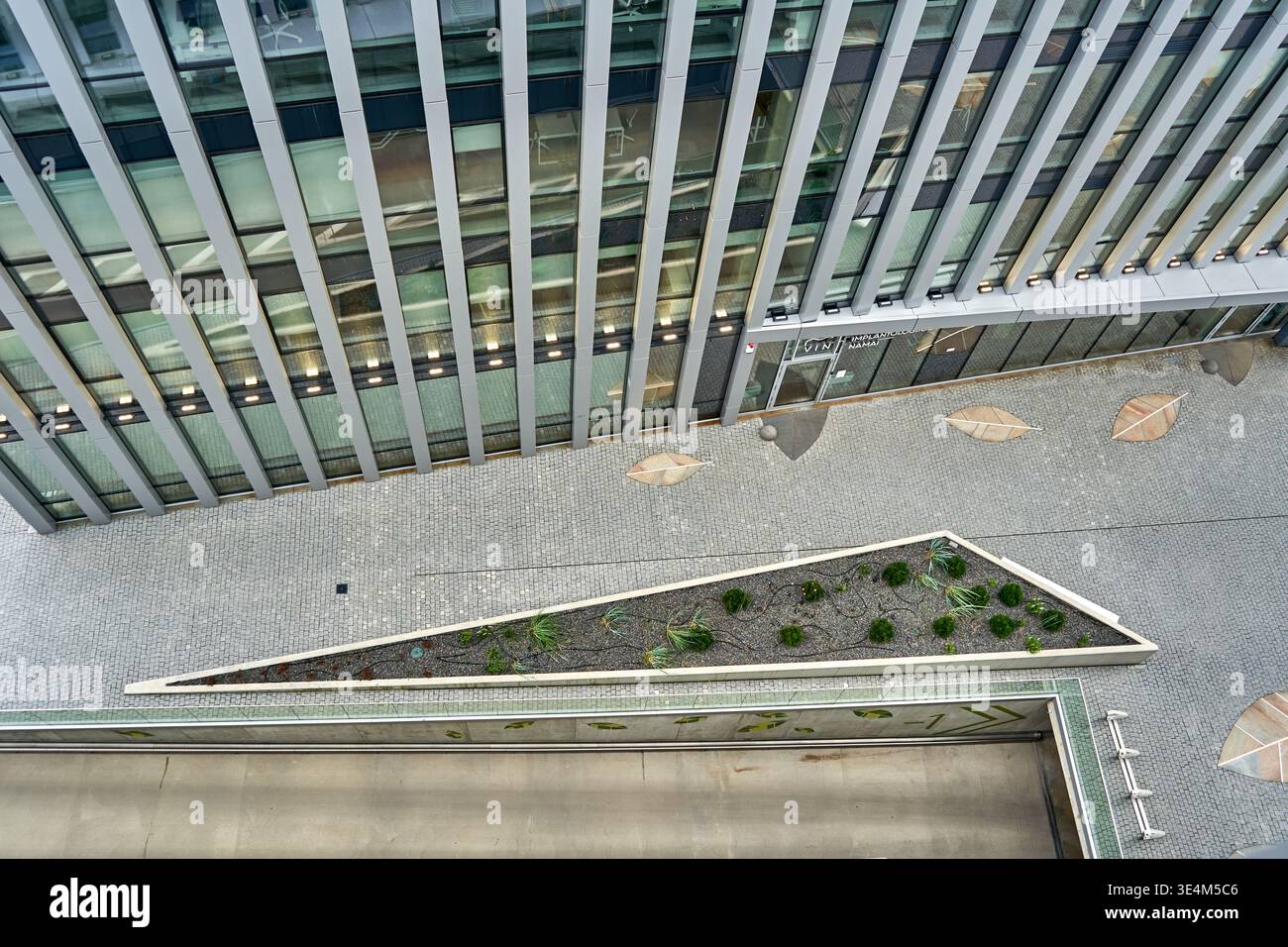 Vista aerea ad alto angolo di un edificio di uffici contemporaneo caratterizzato da una cortina di vetro con montanti verticali in metallo. Il livello del suolo rivela un Foto Stock