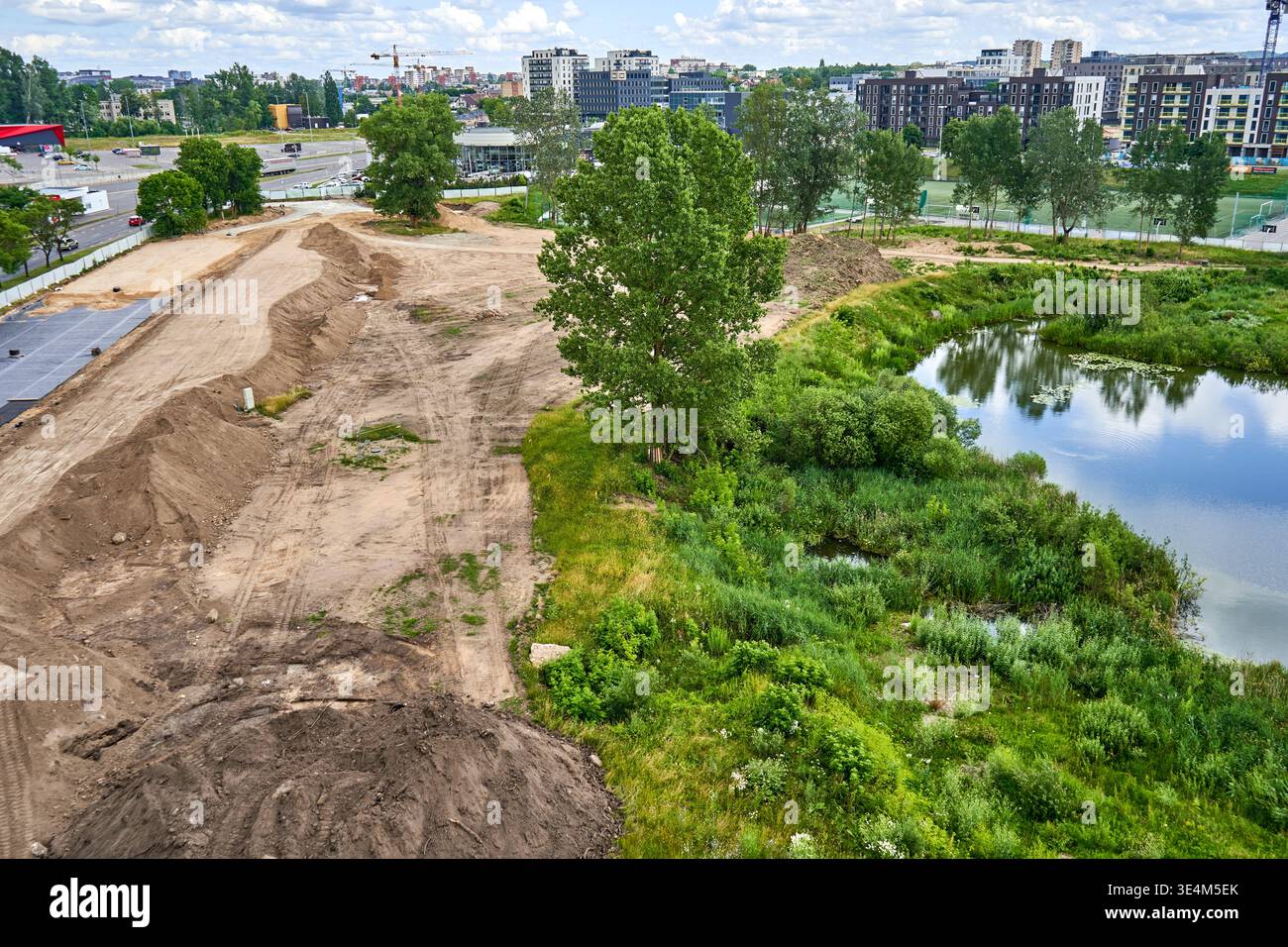 Vista aerea di un cantiere in corso e di un sito di sviluppo del terreno adiacente a un laghetto naturale. La parte sinistra mostra il terreno sgombro con strade sterrate, Foto Stock