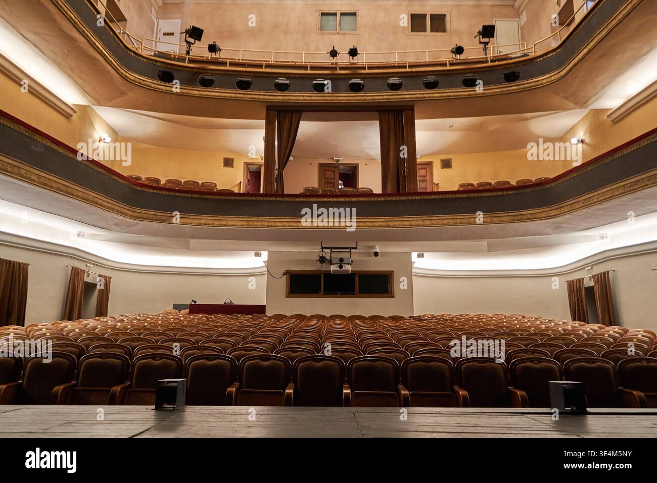 Vista interna di un classico auditorium vuoto catturato dalla prospettiva del palco. L'immagine mostra tre livelli di balconi ornati e. Foto Stock