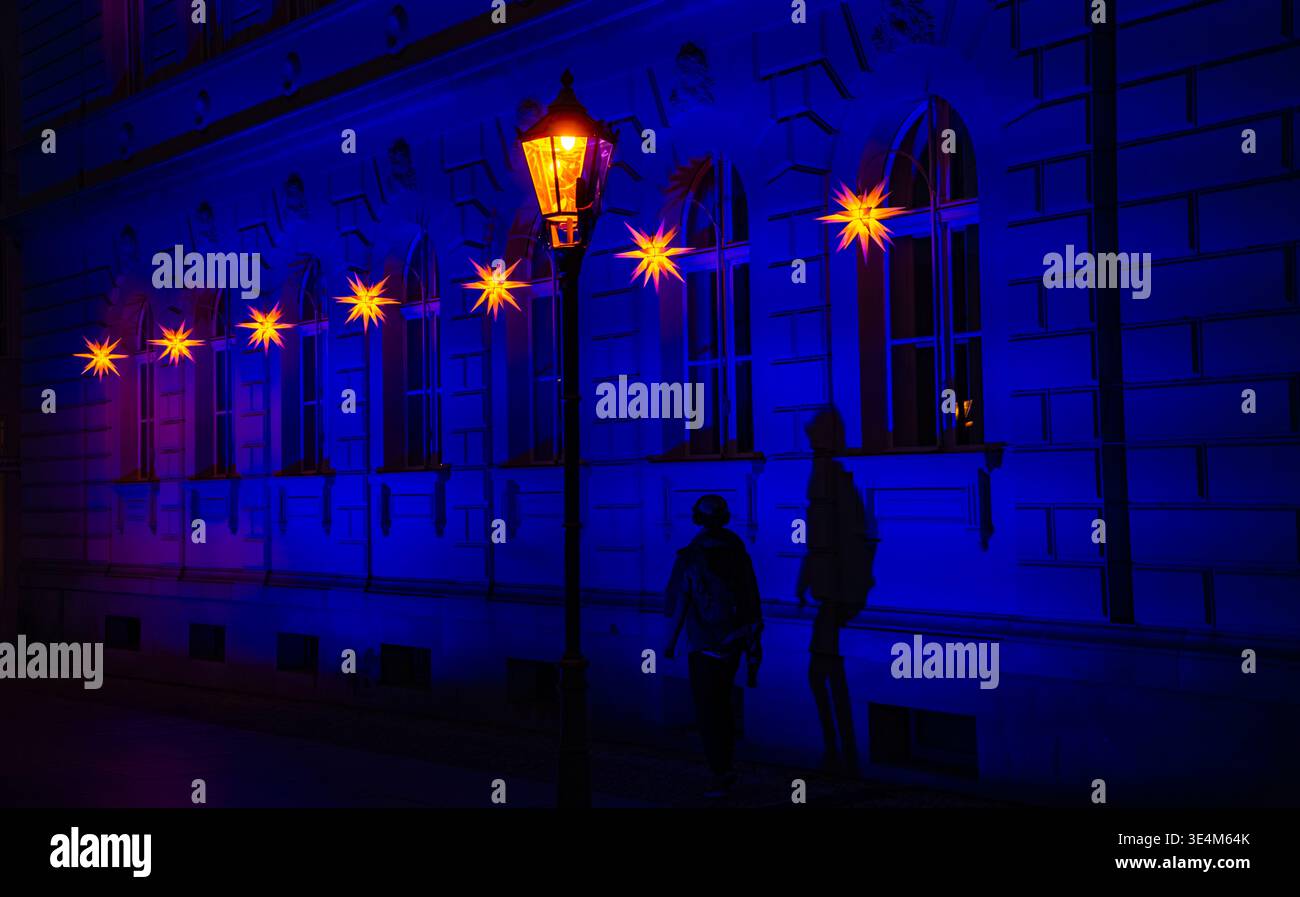 Figura in silhouette e ombra scura sotto luci luminose di stelle di Natale su una facciata di edificio illuminata di blu di notte Foto Stock