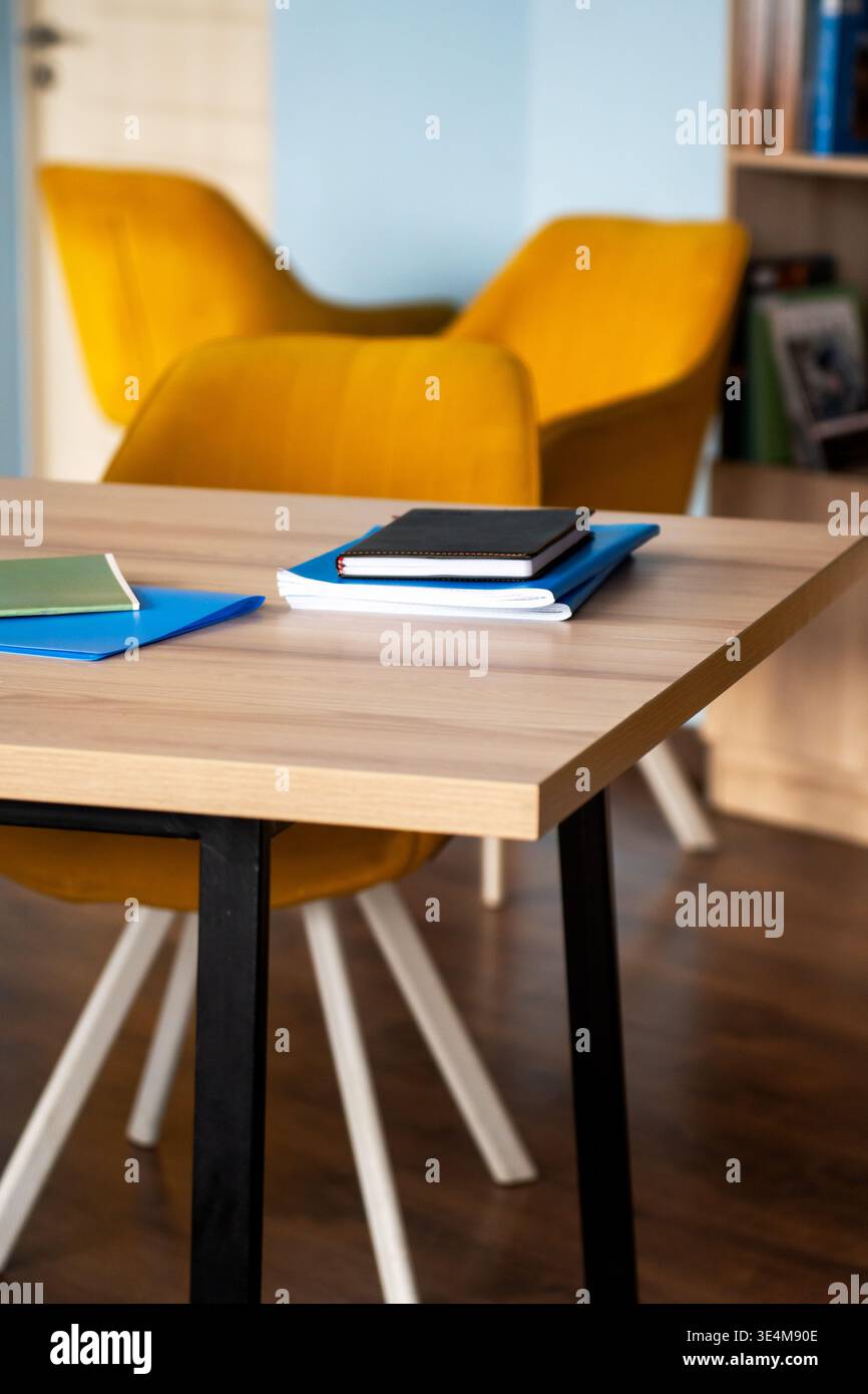 Un accogliente spazio studio con eleganti sedie gialle e materiali da studio organizzati su una scrivania in legno Foto Stock