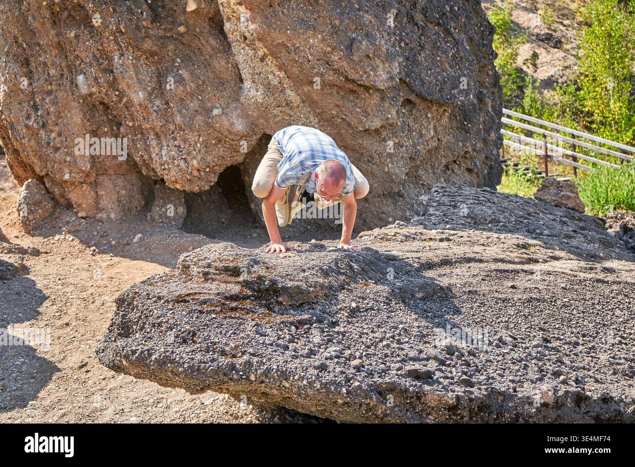 Un uomo adulto più anziano che indossa una camicia a maniche corte a scacchi azzurri, pantaloncini kaki e un berretto piegati con entrambe le mani su una grande testurizzata Foto Stock