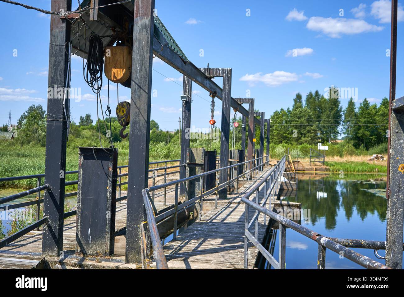 Una struttura industriale di controllo dell'acqua che si estende su un canale calmo in una giornata di sole. L'installazione è dotata di una passerella in legno con agenti atmosferici e metallo Foto Stock