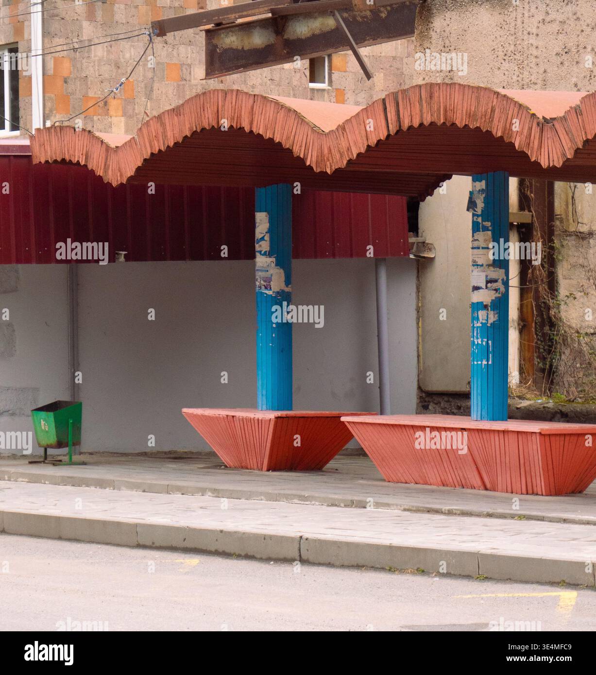 Riparo per autobus con tetto rosso decorativo, colonne blu e vasi sul marciapiede di una tranquilla strada urbana, Alaverdi, Armenia Foto Stock