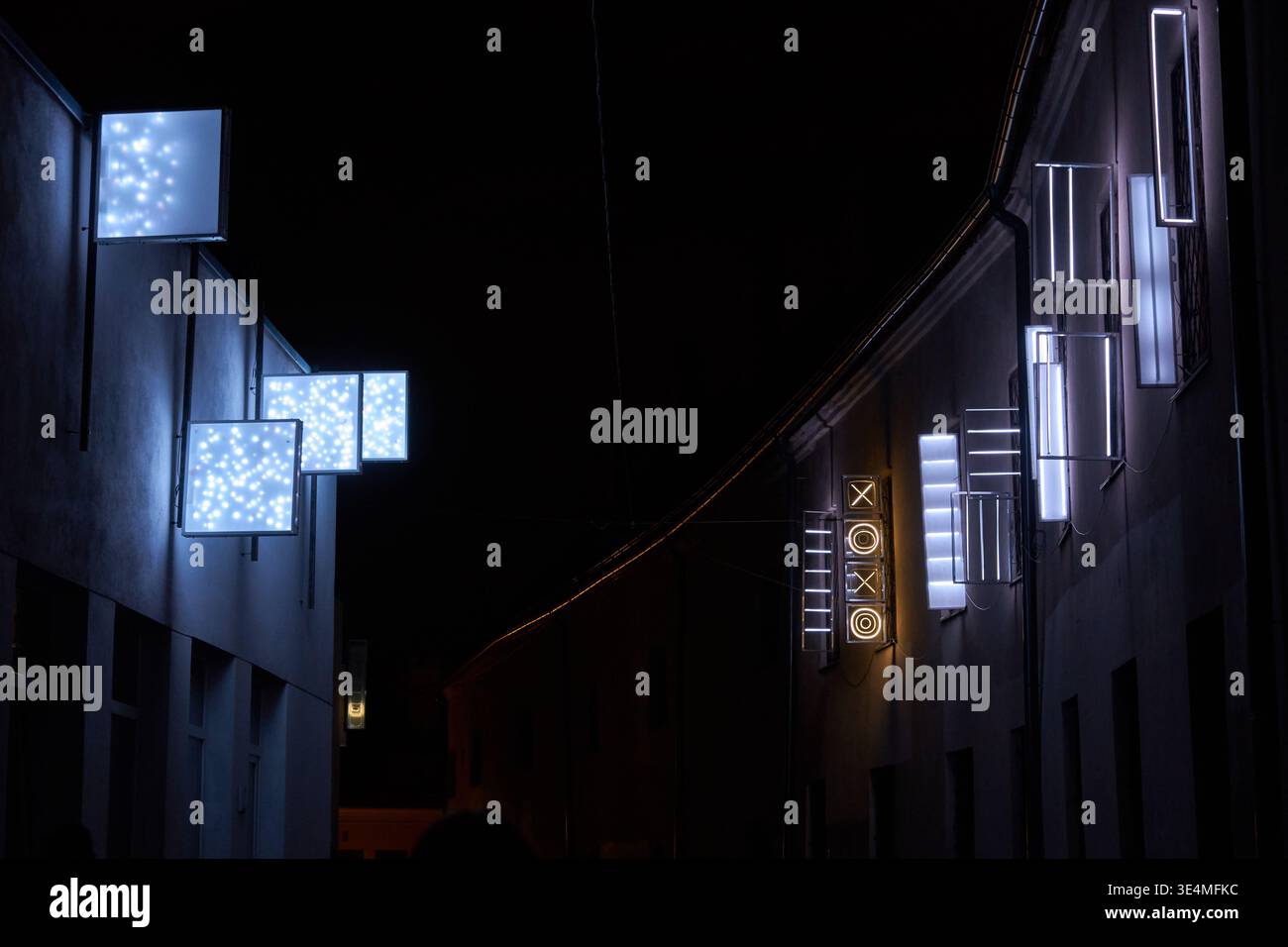 Una scena urbana notturna caratterizzata da moderne installazioni d'arte leggera montate sulle facciate dell'edificio lungo una strada stretta o un vicolo. Nell'edificio di sinistra, Foto Stock