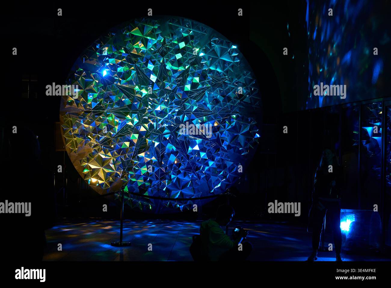 Una grande installazione circolare di light art caratterizzata da una struttura geometrica cristallina composta da numerose sfaccettature triangolari, illuminata con vibrante Foto Stock