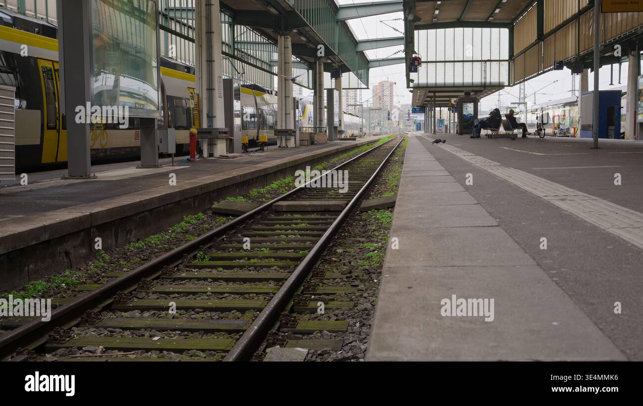 Piattaforma ferroviaria vuota con binari e sfondo urbano, creando una scena di trasporto tranquilla e strutturata. Foto Stock