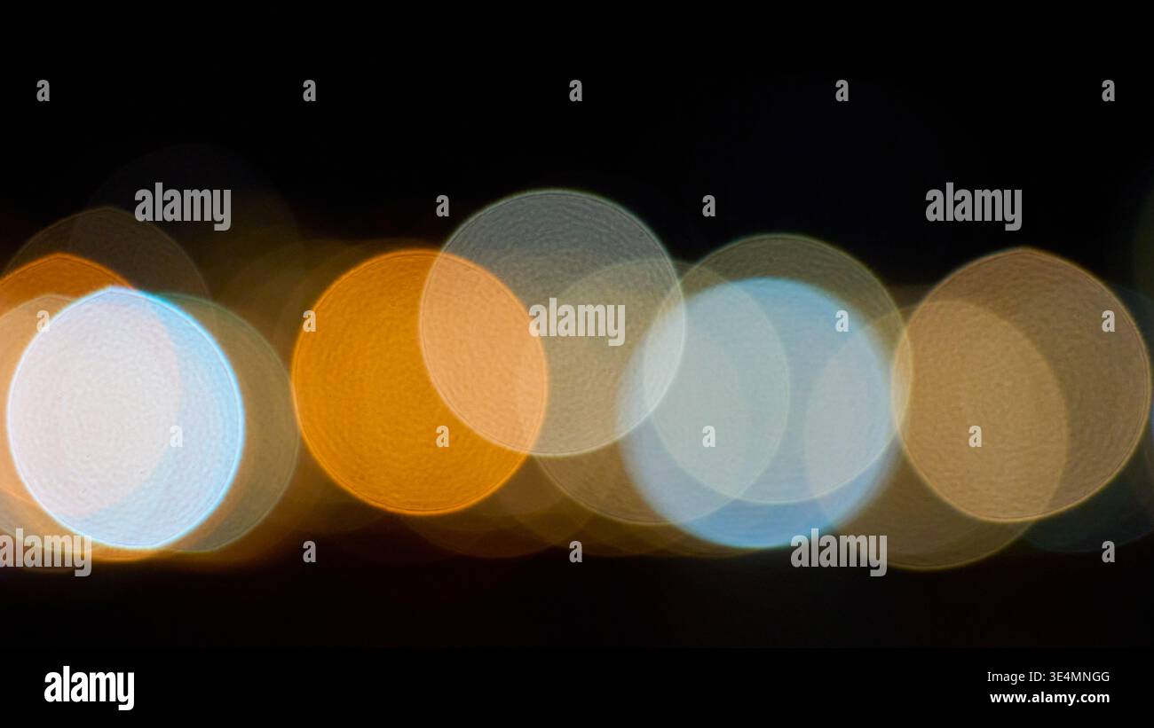 Sfondo notturno astratto con colorate luci bokeh sfocate nei toni arancione, blu e bianco. Forme circolari morbide fuori fuoco su sfondo scuro. Foto Stock
