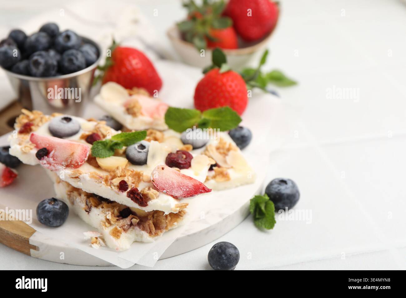 Pezzi di gustosa corteccia di yogurt con frutti di bosco, muesli e menta sul tavolo leggero, primo piano. Spazio per il testo Foto Stock