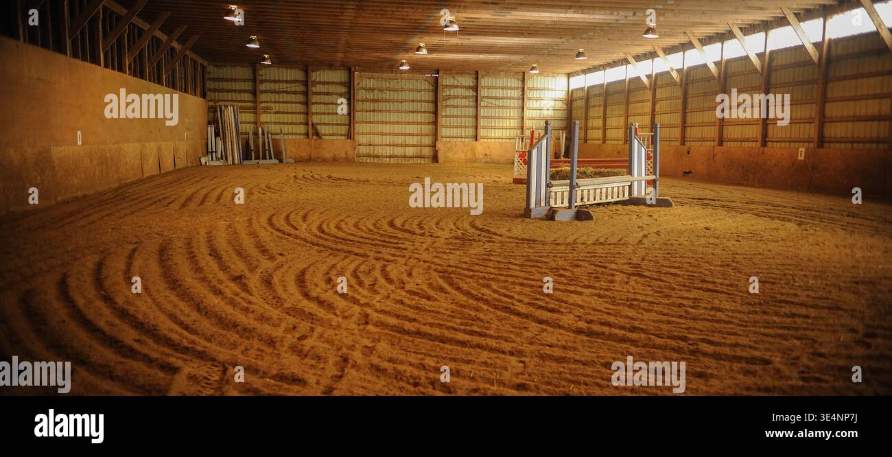 Centro di equitazione al coperto con salti e finestre con piedi erbosi che lasciano entrare luce, grande arena al coperto per equitazione presso la struttura di equitazione Foto Stock