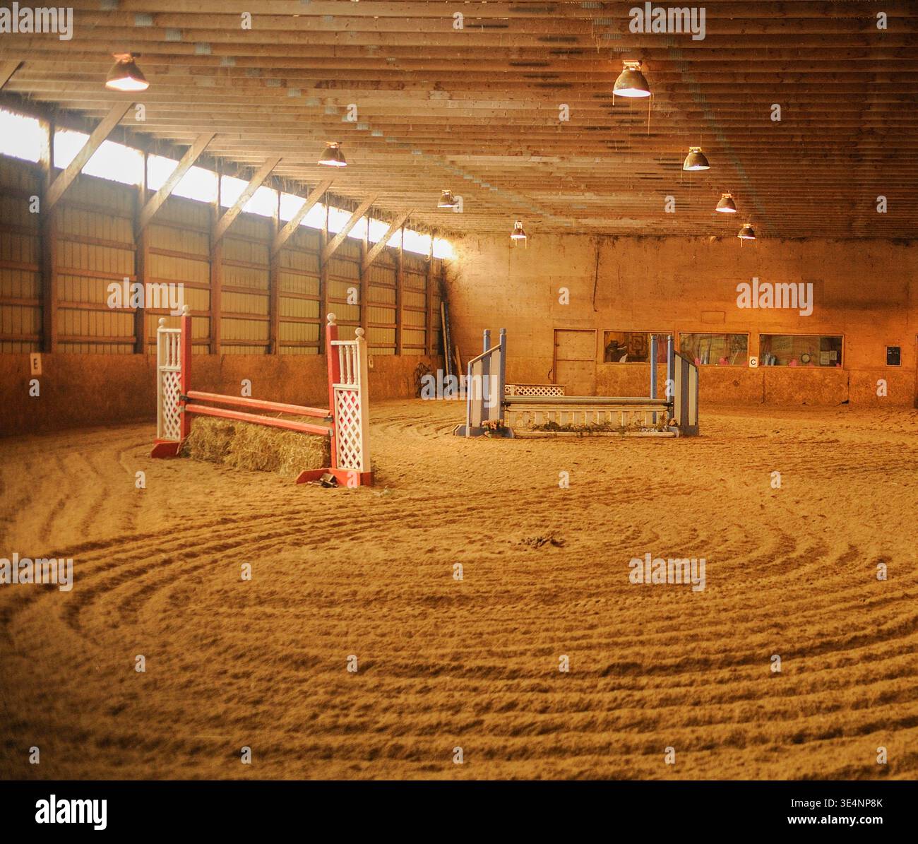 Centro di equitazione al coperto con salti e finestre con piedi erbosi che lasciano entrare luce, grande arena al coperto per equitazione presso la struttura di equitazione Foto Stock