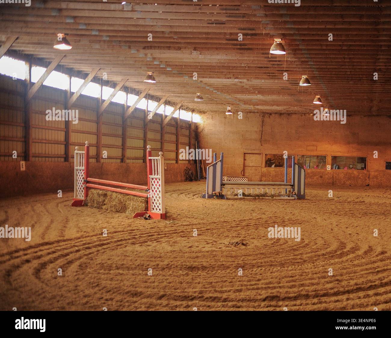 Centro di equitazione al coperto con salti e finestre con piedi erbosi che lasciano entrare luce, grande arena al coperto per equitazione presso la struttura di equitazione Foto Stock