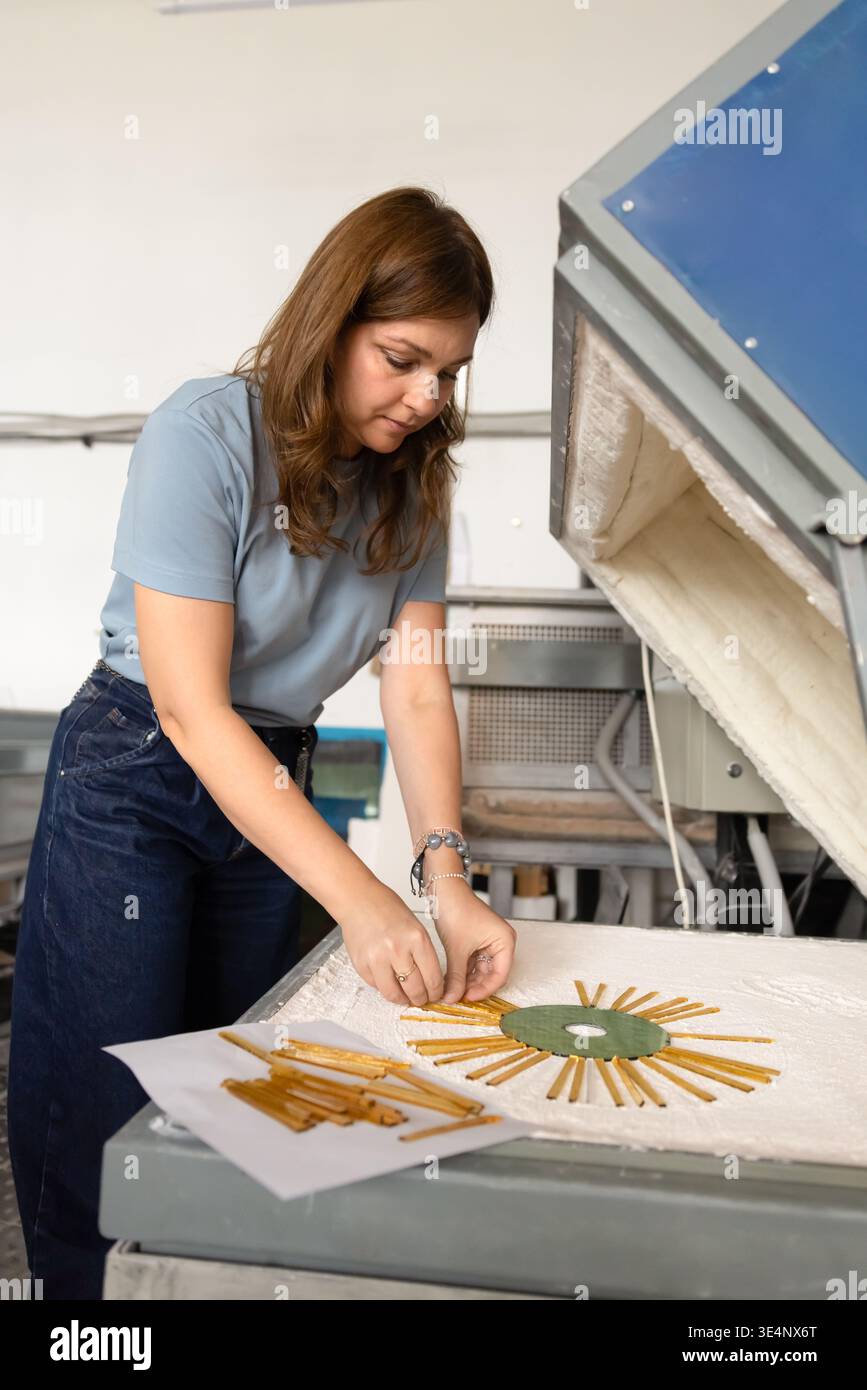 Artigiana che organizza pezzi di vetro su forno in laboratorio Foto Stock