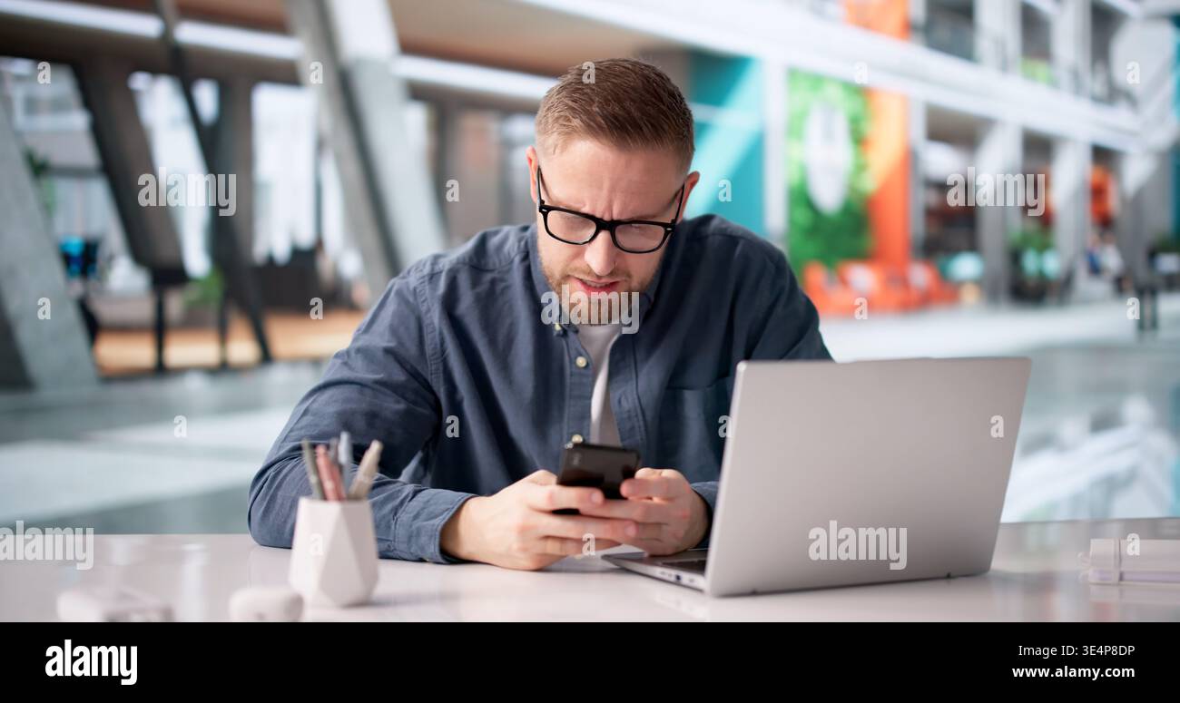 L'uomo esamina con ansia lo smartphone per individuare eventuali problemi di pagamento durante l'impostazione della conferenza Foto Stock