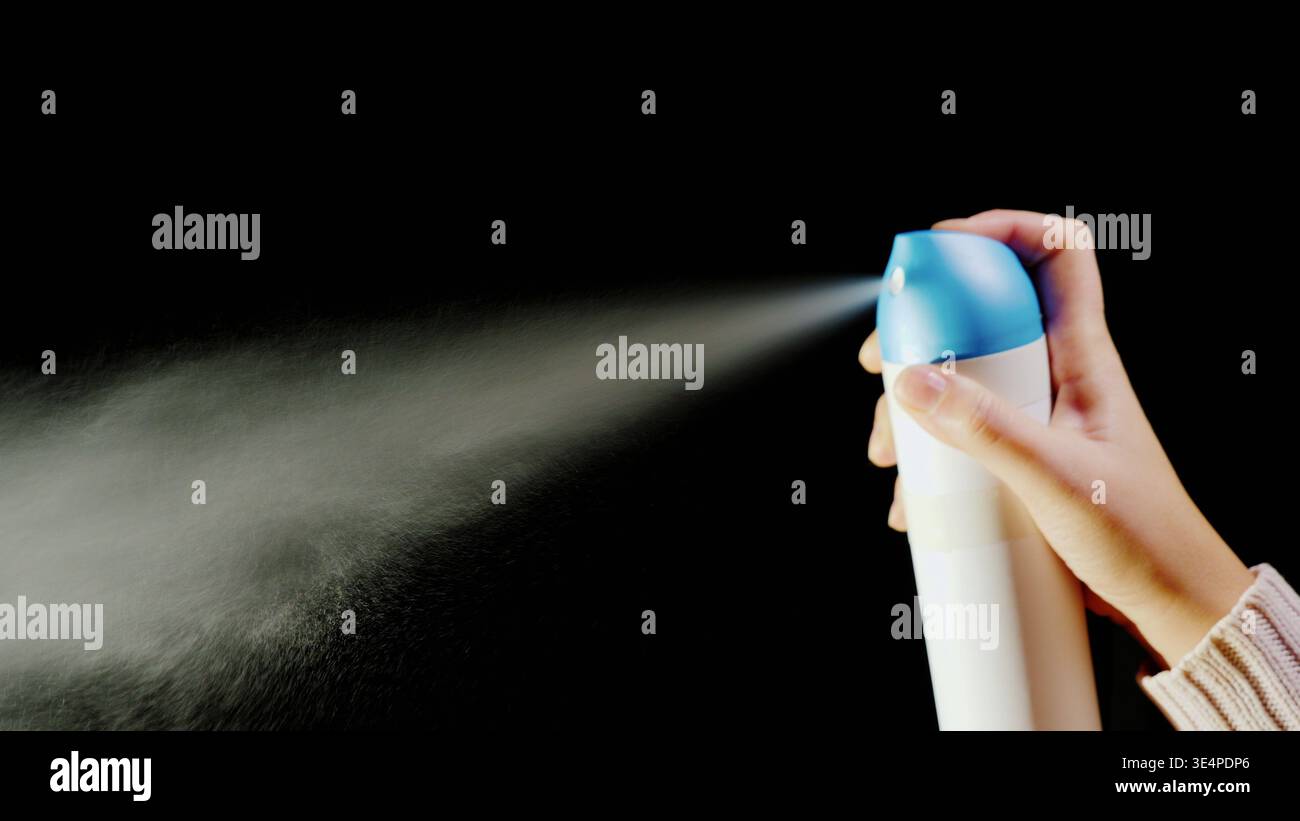 Mano con bomboletta aerosol. Spruzzare lo spray su sfondo nero Foto Stock