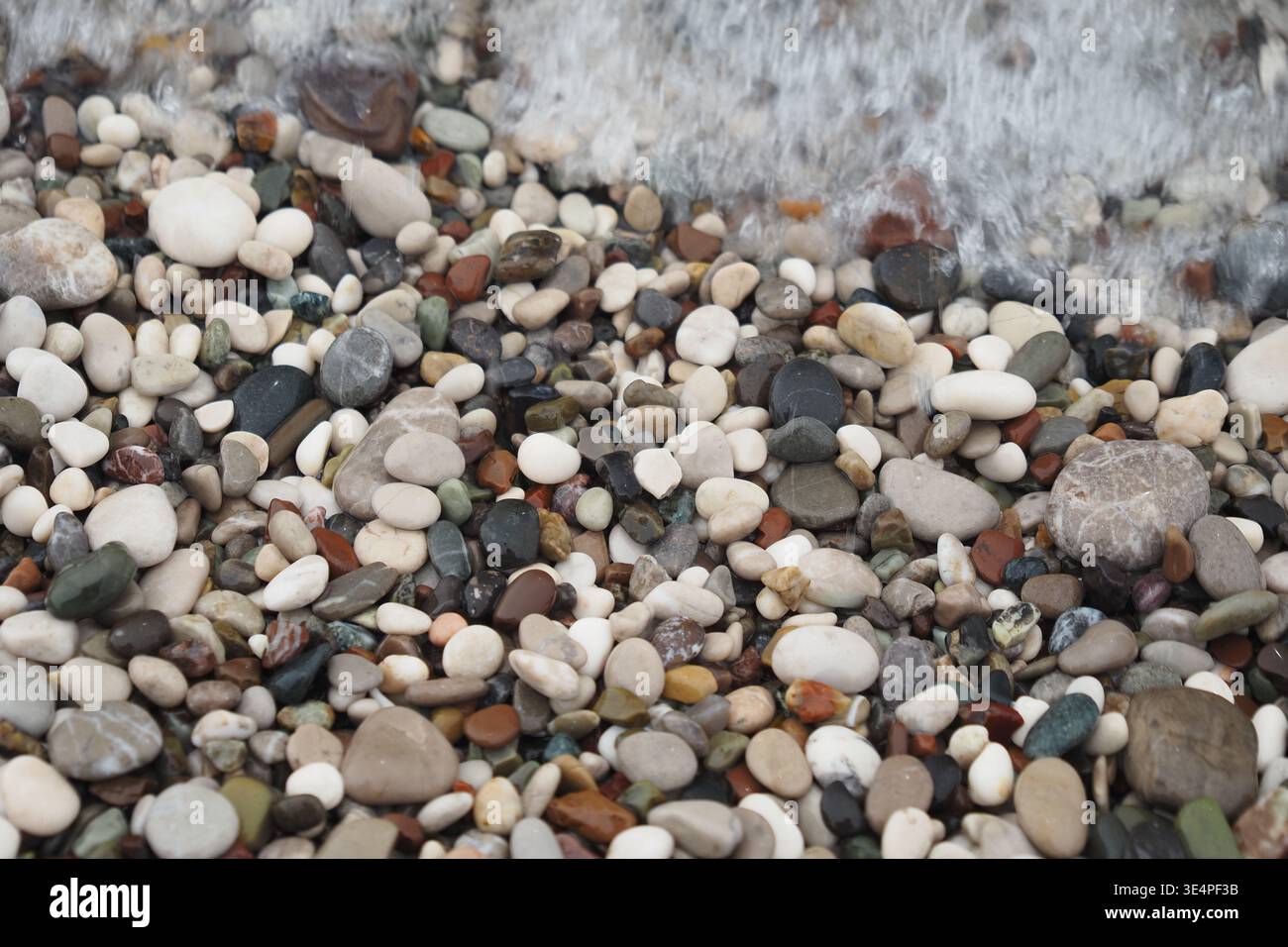 Ciottoli su una spiaggia con onde che spruzzano al tramonto Foto Stock