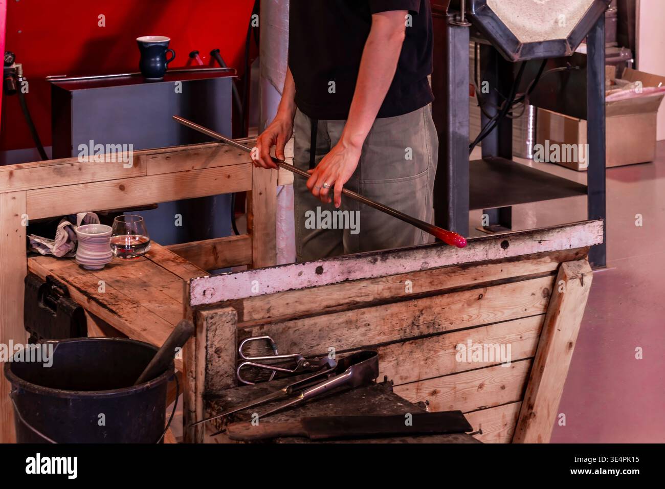 Creazione di opere d'arte in vetro. Artigianato artigianale con vetro fuso ardente in un ambiente da studio grintoso. Artigiani mirati modellano sapientemente il vetro luminoso utilizzando utensili Foto Stock
