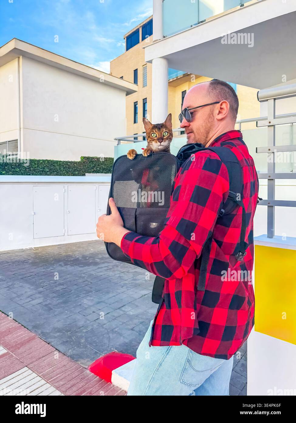 Legame urbano con gli animali domestici. Uomo con zaino per gatti in città. Ritratto informale del proprietario con animale domestico in una strada trafficata. Gatto da trasporto individuale rilassato in città Foto Stock