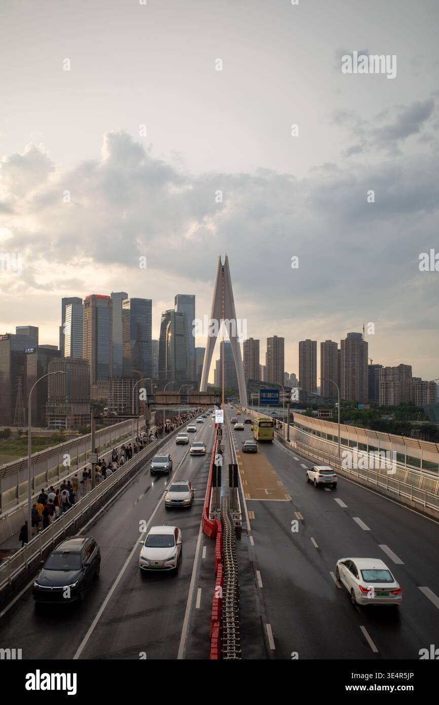 Il ponte urbano attraversa lo skyline della città al crepuscolo. Le vetture si muovono lentamente su superfici bagnate di asfalto. I moderni grattacieli sorgono dietro il ponte. Sky mostra le nuvole contro Foto Stock
