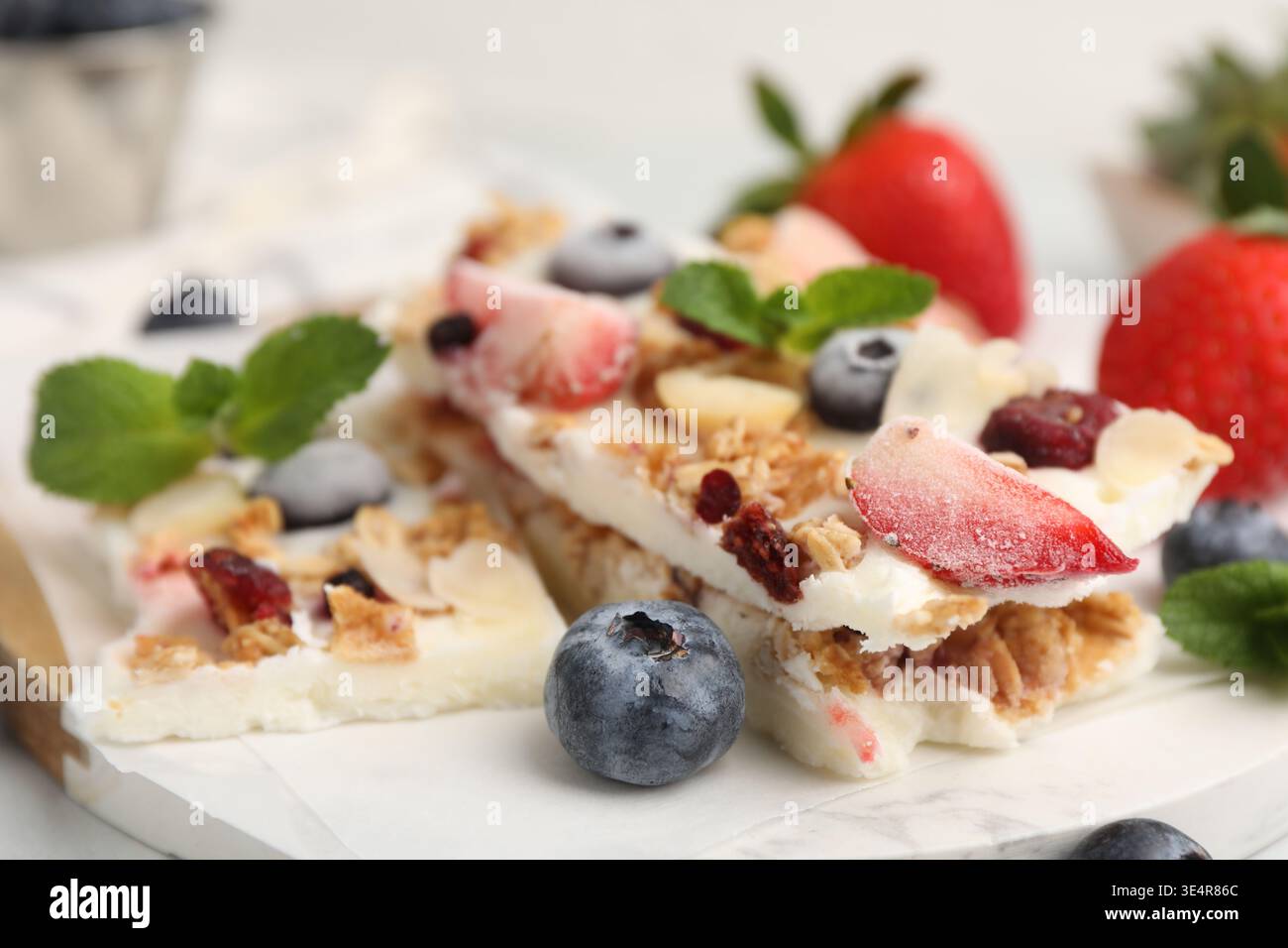 Pezzi di gustosa corteccia di yogurt con frutti di bosco, muesli e menta sul tavolo leggero, primo piano Foto Stock