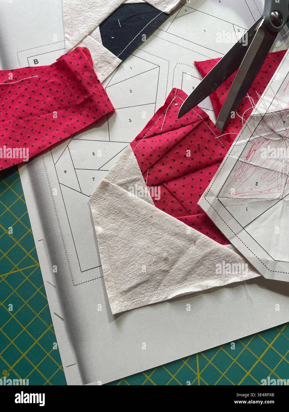 Primo piano del blocco trapuntato FPP (Foundation Paper Piecing) in corso con tessuto a pois rosso, motivi di carta e forbici su un tappetino da taglio Foto Stock