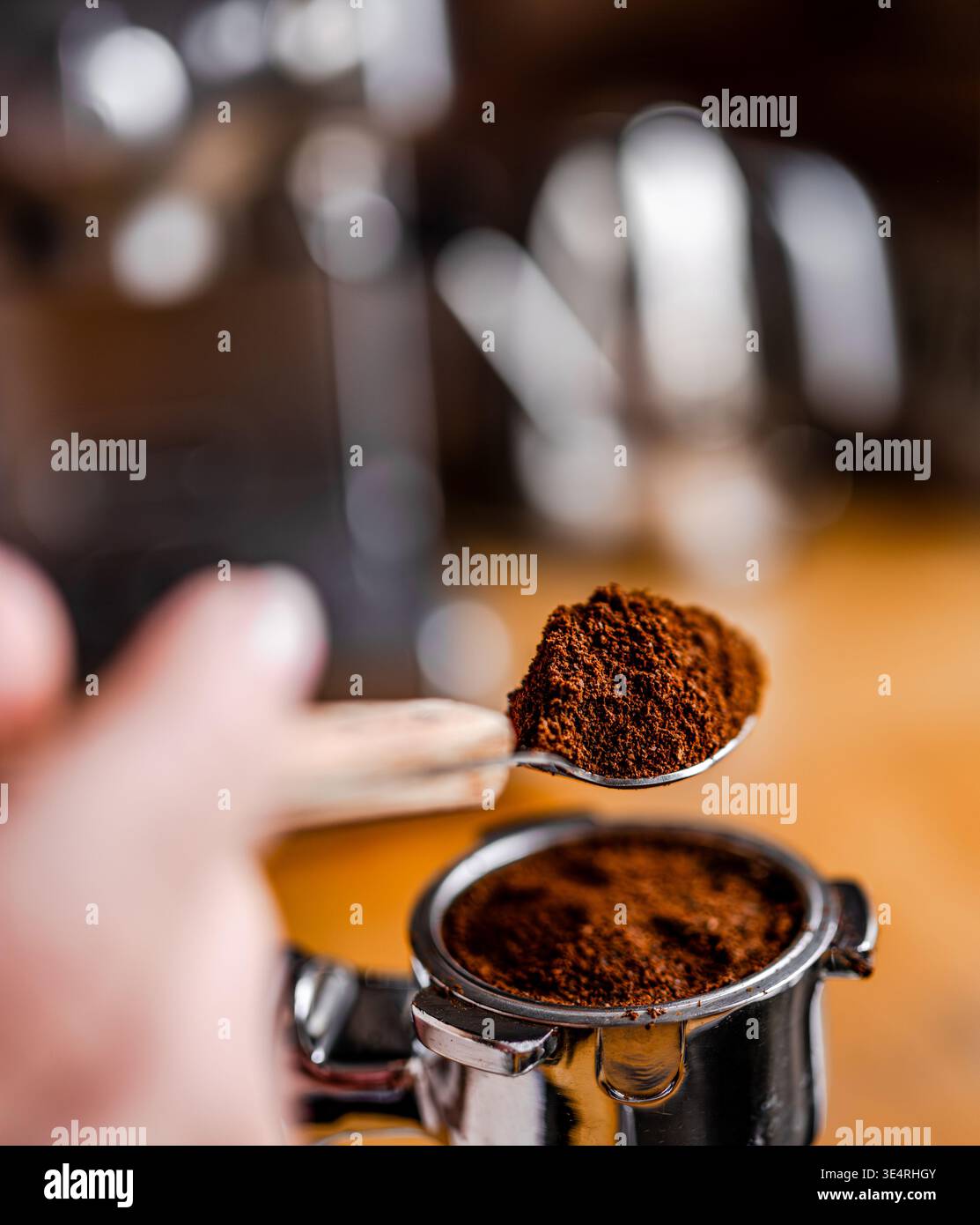 Primo piano di una donna che versa il caffè in un portafiltro della macchina da caffè con una mano visibile Foto Stock