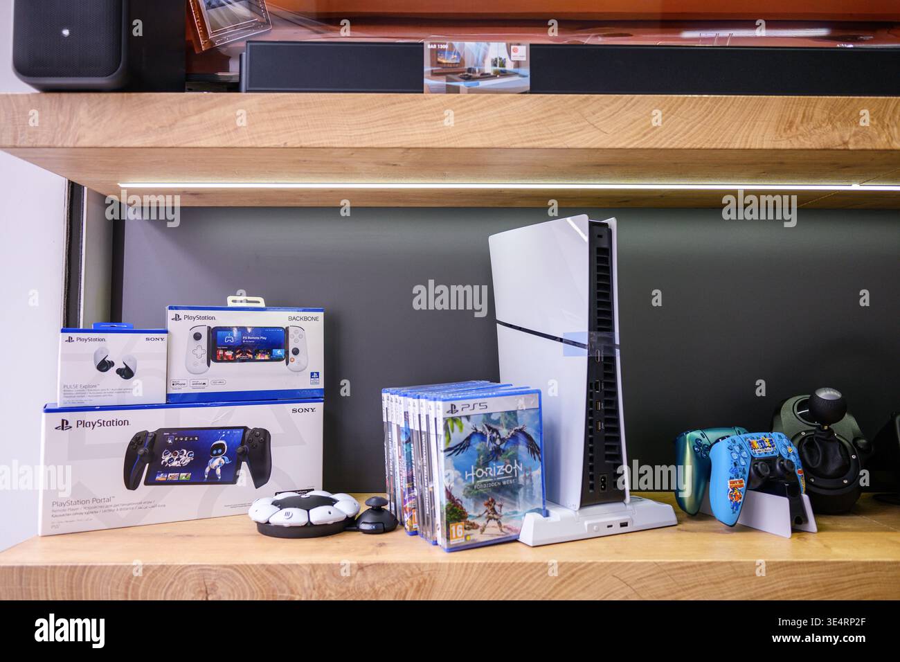 Moderno sistema di gioco con console e accessori. Ripiani in legno puliti che mostrano vivaci scatole di gioco. I dispositivi mostrano un'atmosfera giocosa e incentrata sulla tecnologia. Idea Foto Stock