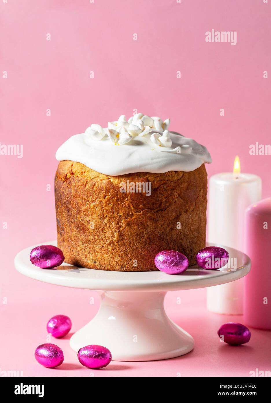 Festiva la natura morta di Pasqua con il tradizionale kulich ricoperto di glassa bianca e fiori di marshmallow, circondato da uova di cioccolato e candele accese Foto Stock