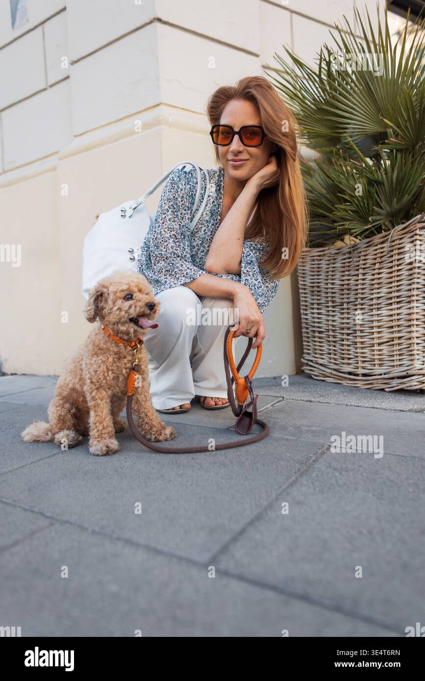 Una giovane donna dona acqua al suo cane sete in una strada cittadina. Vibrazioni urbane estive, cura degli animali domestici e compagnia all'aperto catturati in un momento sincero. Foto Stock
