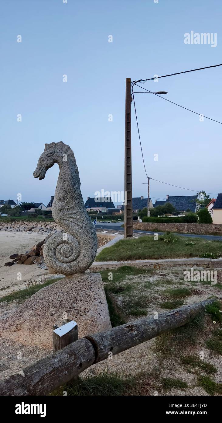 Scultura in pietra di un cavalluccio marino vicino a una spiaggia sotto un cielo tranquillo, situata in un ambiente costiero calmo. Foto Stock