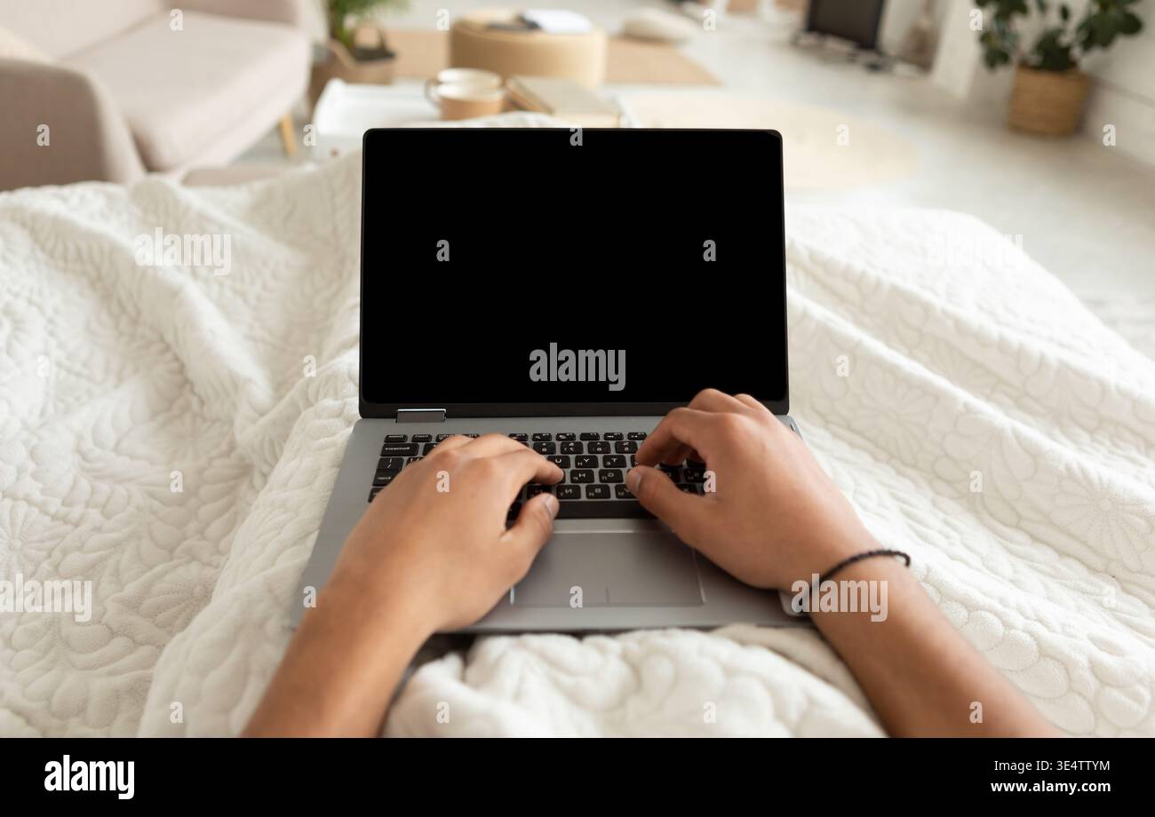 Scatto corto dell'uomo usando il laptop che lavora sdraiato nella camera da letto Foto Stock