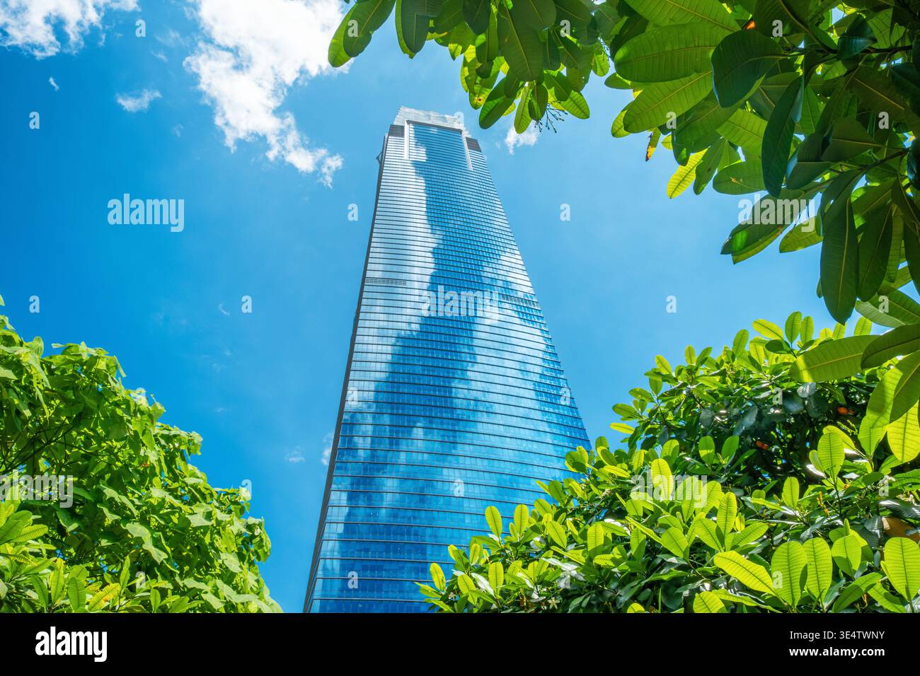 Moderno grattacielo di vetro nella città di Kuala Lumpur con riflessi di nuvole circondato da vegetazione tropicale. Sviluppo urbano e progettazione sostenibile delle città Foto Stock