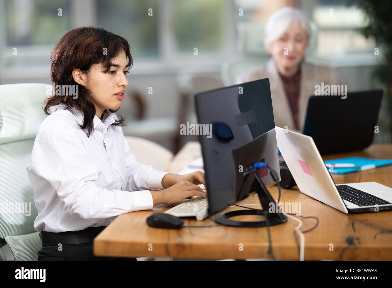 Giovane donna seduta alla scrivania e a scrivere su un computer portatile in un ufficio moderno Foto Stock