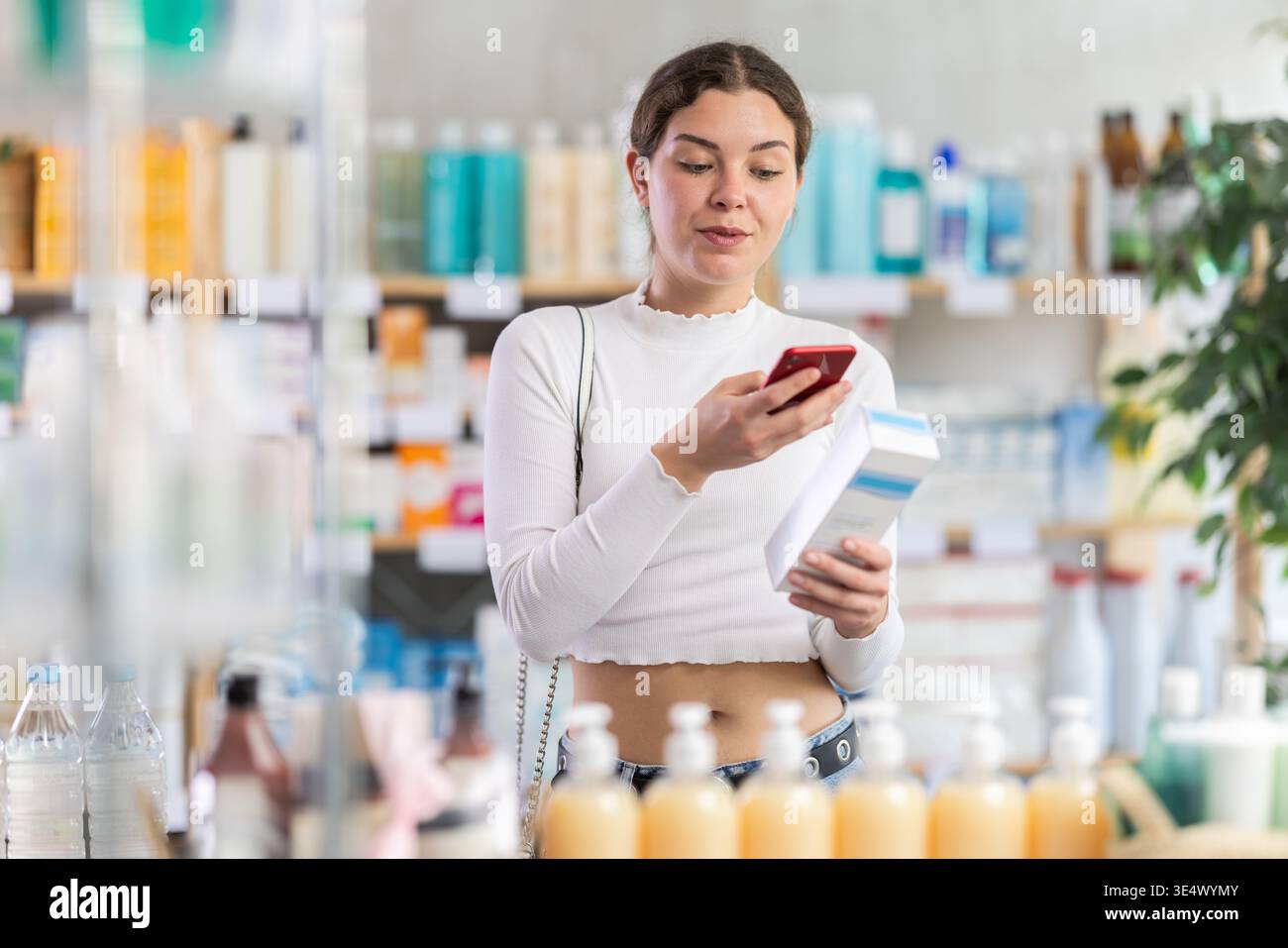Ragazza in abiti estivi scansiona il codice sulla confezione della crema per controllare la data di scadenza Foto Stock
