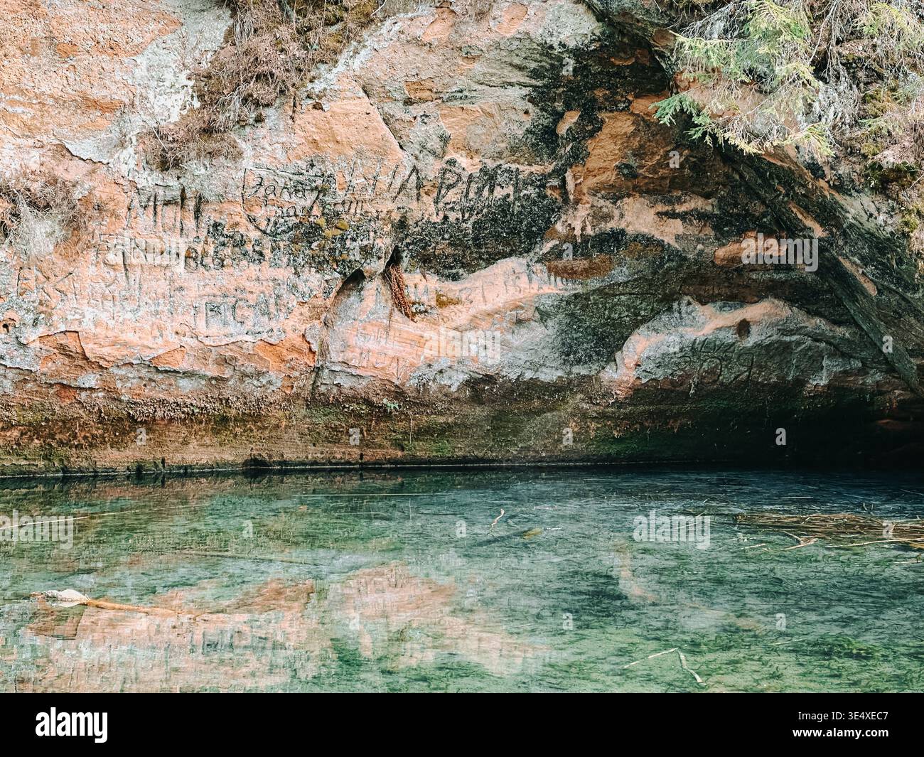 Vista dettagliata di una parete rocciosa della grotta con graffiti riflessi in acque cristalline. Paesaggio naturale ma alterato dall'uomo, ideale per temi di e Foto Stock